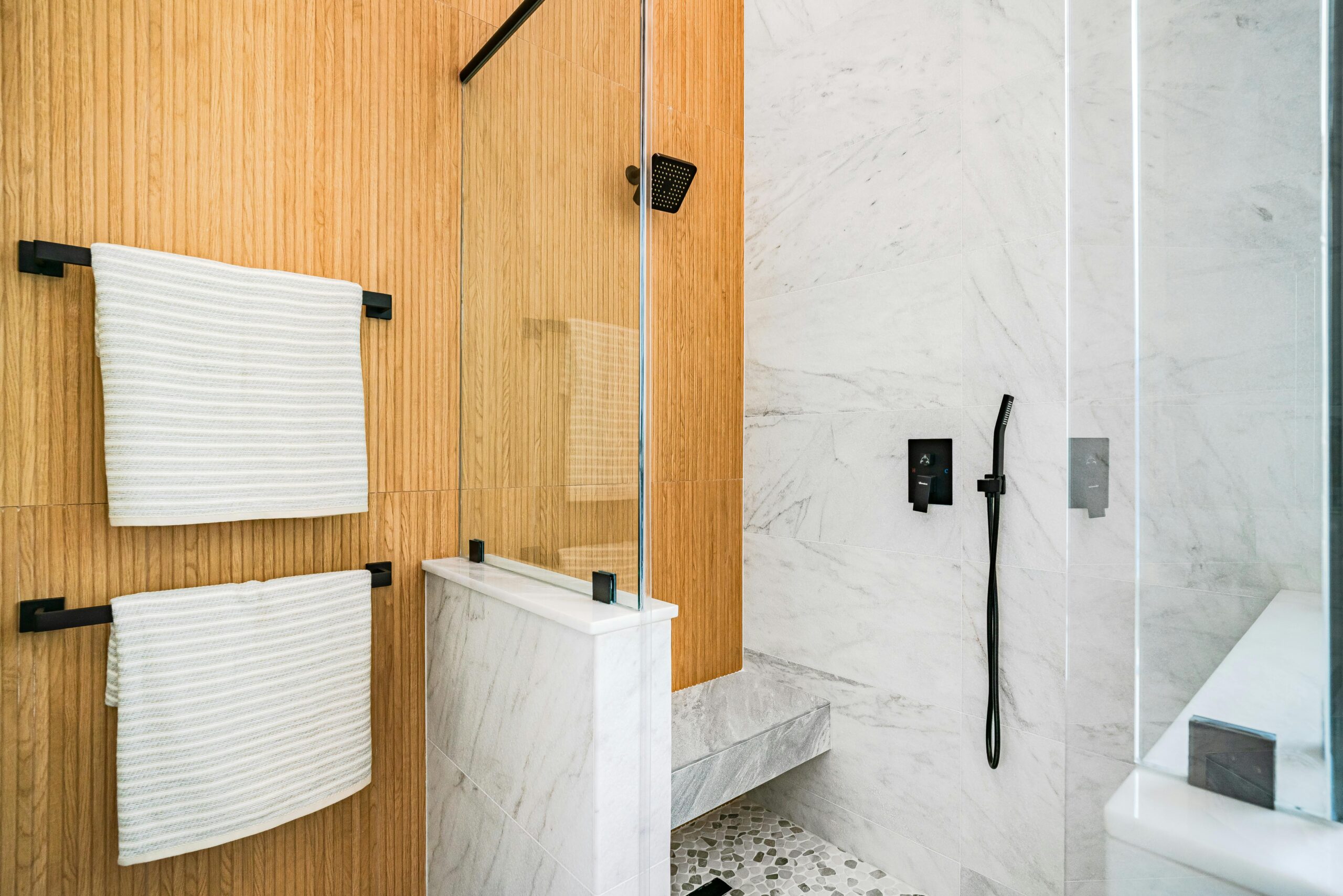 Projects Elegant modern bathroom featuring marble tiles, wood paneling, and glass shower door.